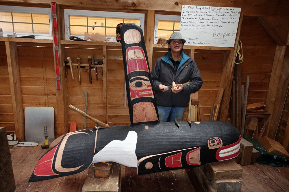 Native Alaskan with totem pole carving of a killer whale